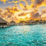 Bungalows sur pilotis dans un lagon turquoise au coucher du soleil