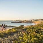 Couple cycling along a coastal path near a beach.